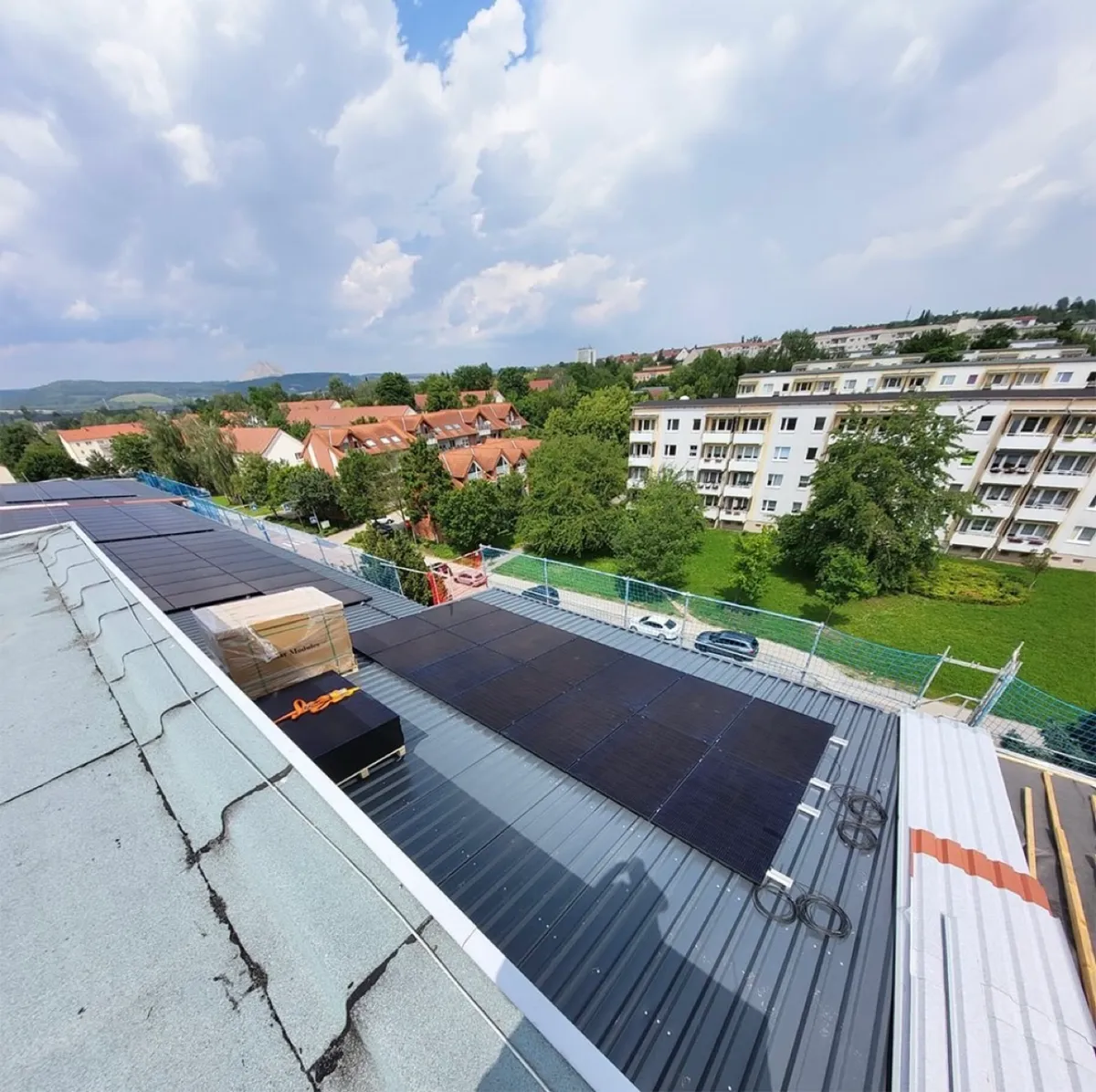 Schwarze Photovoltaikmodule auf dem Blechdach eines großen Gebäudes, daneben Modulpaletten